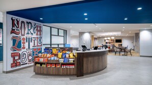 A hotel reception area with a counter displaying snacks and a large wall with the hotel's name. - Tru by Hilton North Little Rock (North Little Rock)