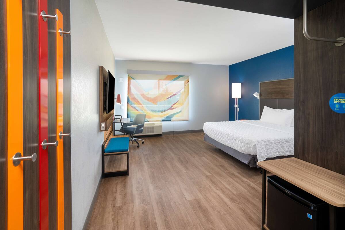 Habitación de hotel con cama, escritorio, silla y televisión montada en la pared.