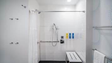 A modern shower area with a glass door, a white tiled wall, a black floor, and a small bench with a towel.
