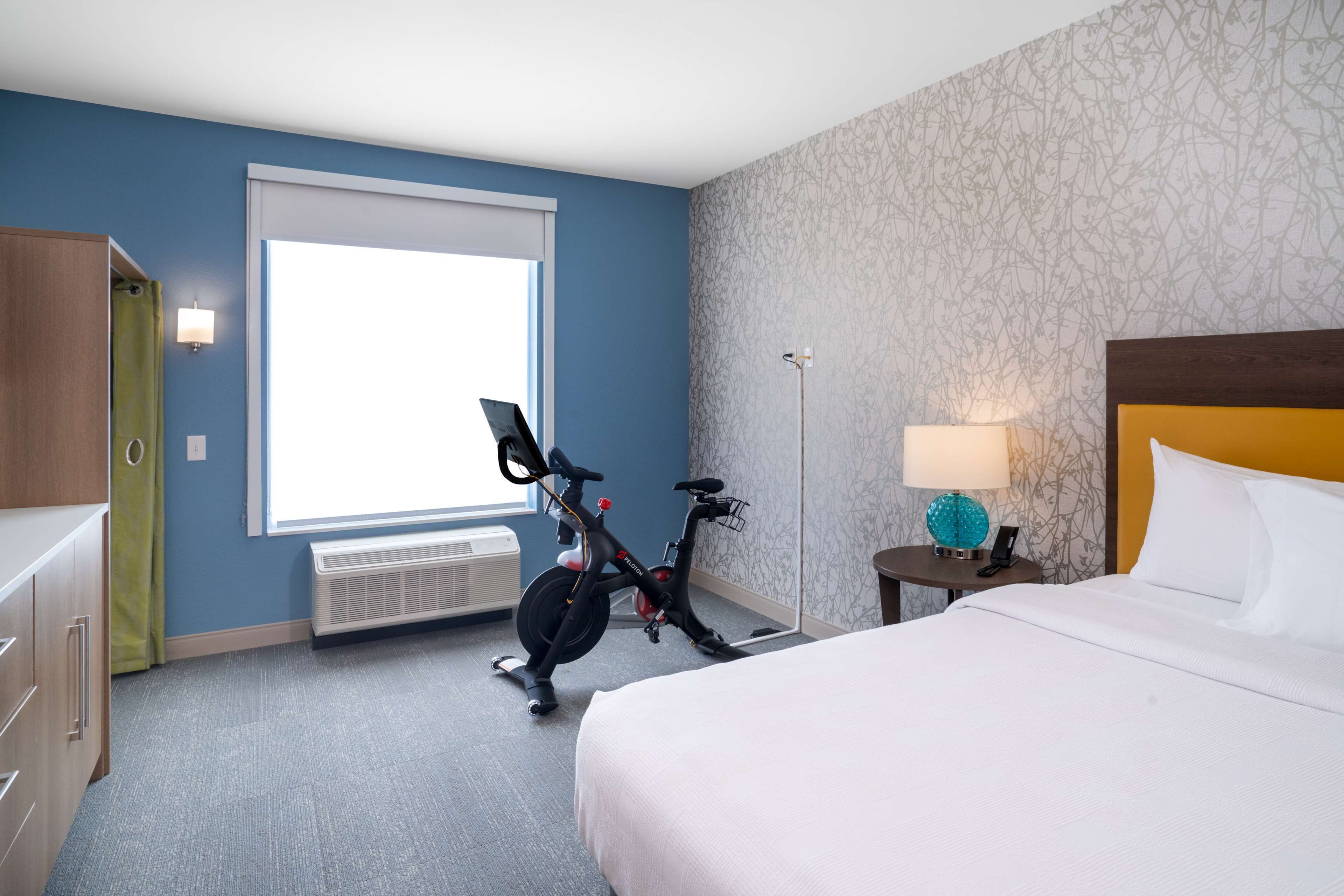 Habitación de hotel con cama, bicicleta, escritorio con lámpara y ventana con persianas.