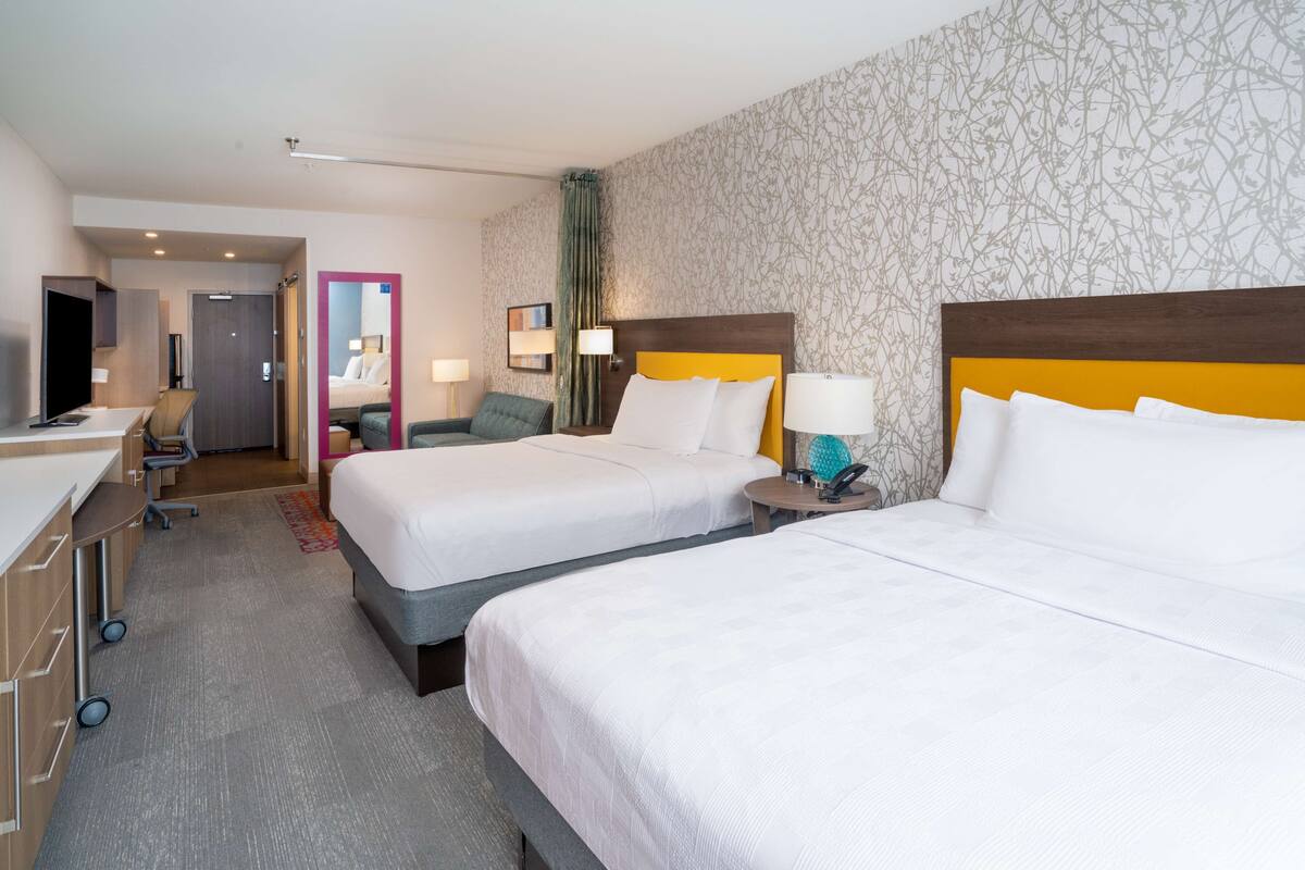 Habitación de hotel con dos camas, un escritorio, una silla y un baño visible a través de una puerta abierta.