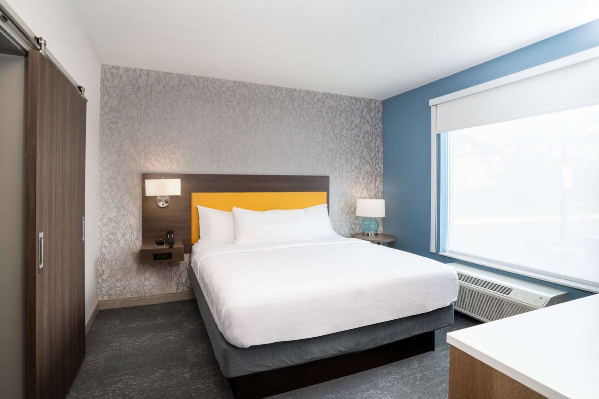 Una habitación de hotel con cama, mesitas de noche, un armario y una ventana.