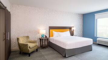 A hotel room with a bed, a chair, a nightstand with a lamp, and a window.