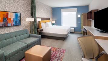 A hotel room with a bed, a sofa, a desk, a television, and a cityscape painting on the wall.