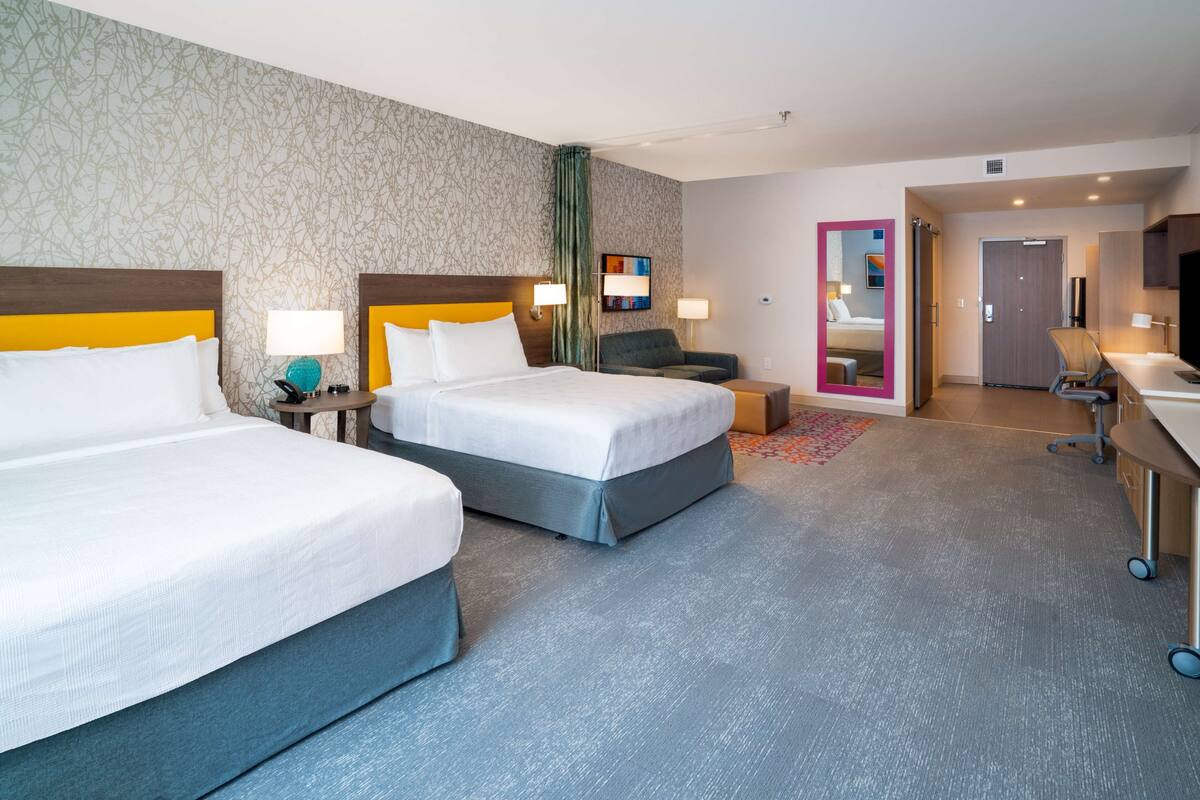 Habitación de hotel con dos camas, un escritorio, una silla, un televisor y un baño.