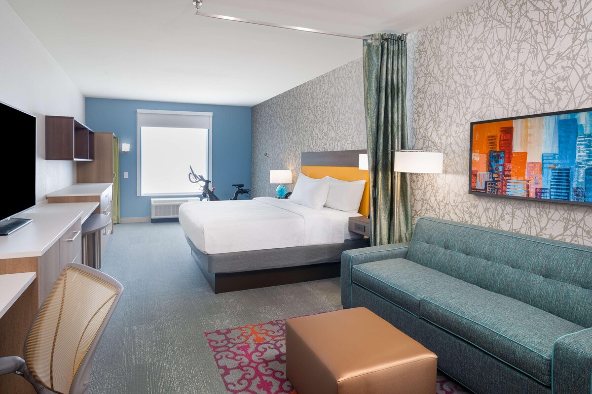 Habitación de hotel con cama, escritorio, silla, sofá y una pintura de un paisaje urbano.