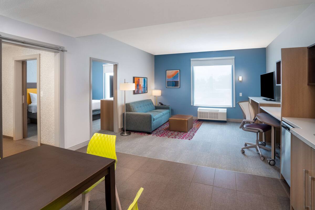 Una habitación de hotel moderna con comedor, sofá, televisor y escritorio.