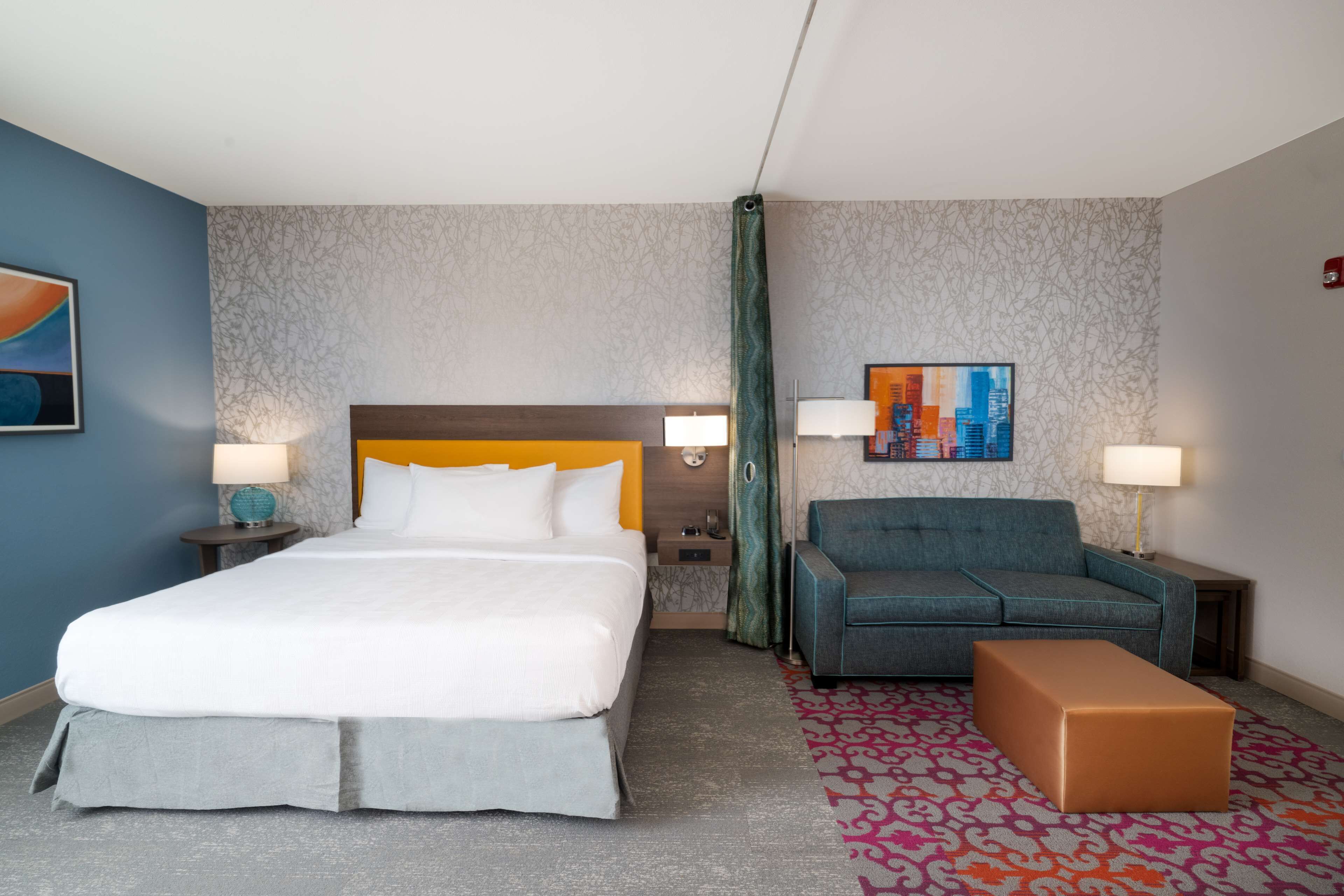Habitación de hotel con cama, sofá, una mesita y alfombra estampada.