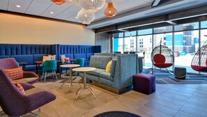 A modern lounge area with seating arrangements, including sofas and chairs, and a large window providing a view of the outside. - Tru by Hilton Rocky Mount (Rocky Mount)