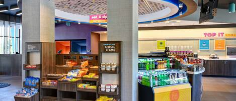 A 24/7 market area with a variety of food and drink options, including a refrigerated section and a snack display.