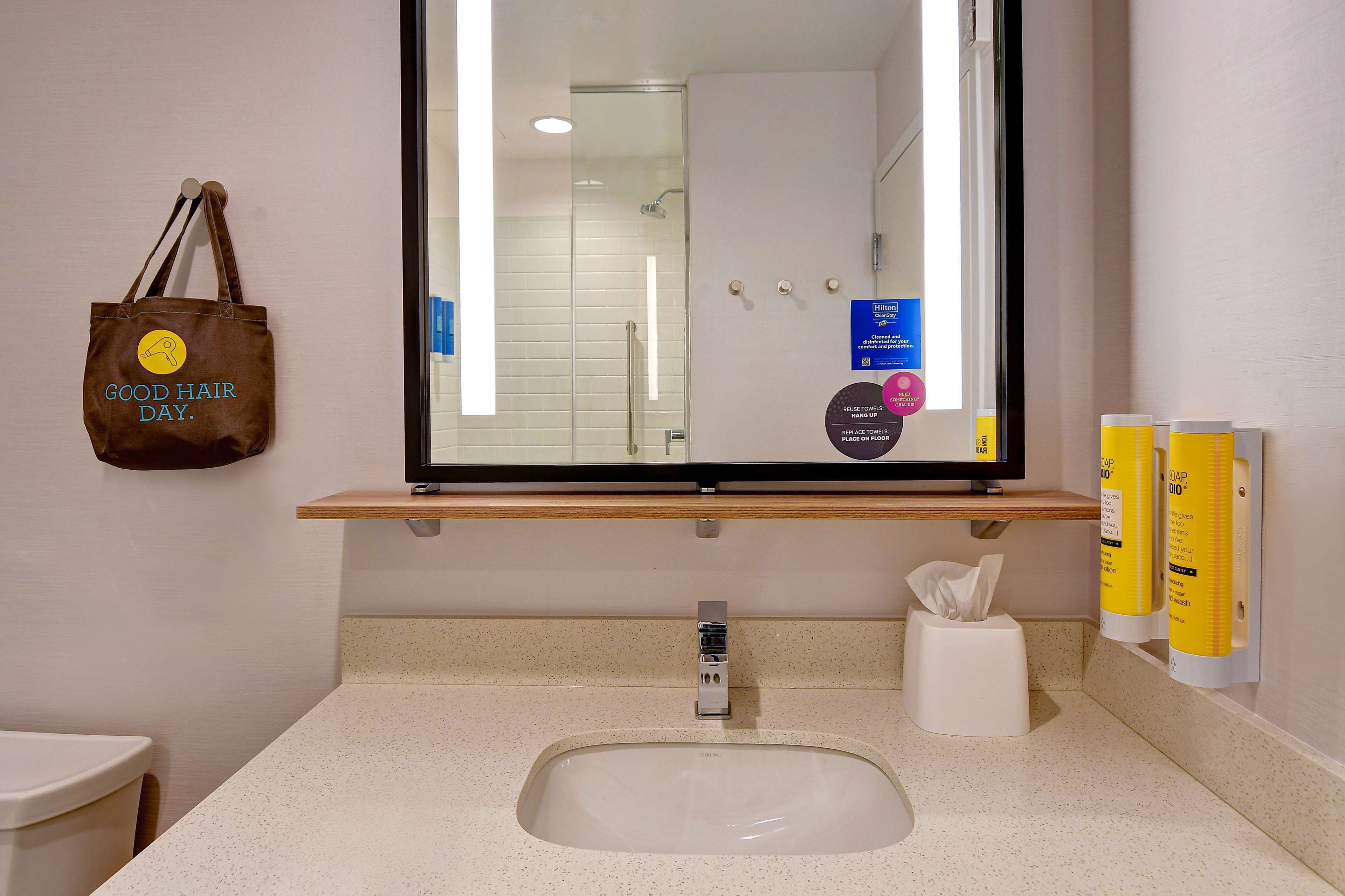 A bathroom with a sink, mirror, towel dispenser, and a hand dryer.