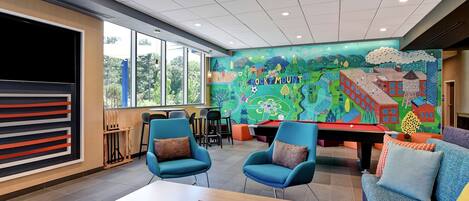 A modern lounge area with blue chairs, a pool table, and a colorful mural depicting a landscape with the text "Rock Mount".