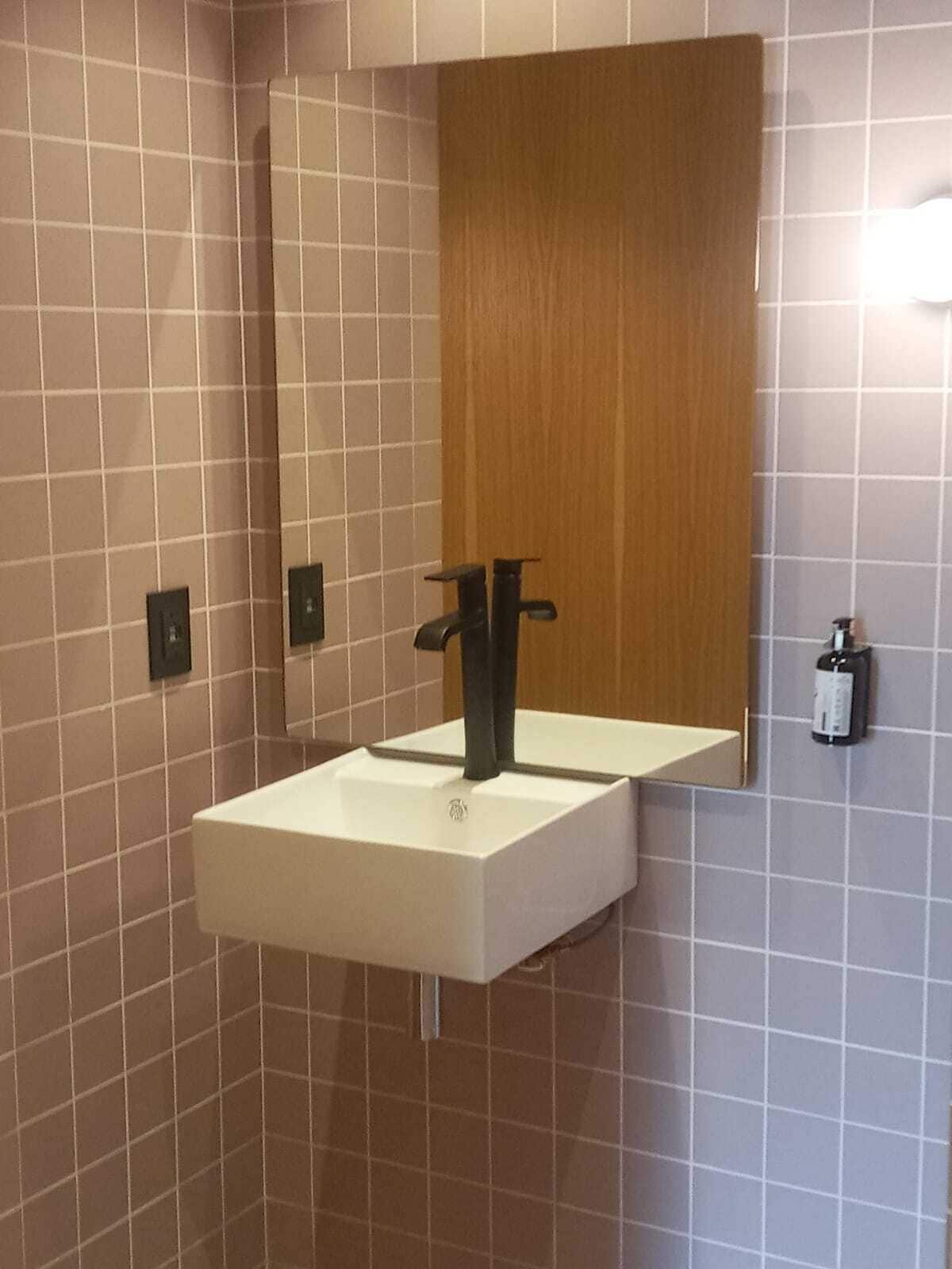 Une salle de bain avec un lavabo blanc, un miroir et un panneau en bois au-dessus du miroir.