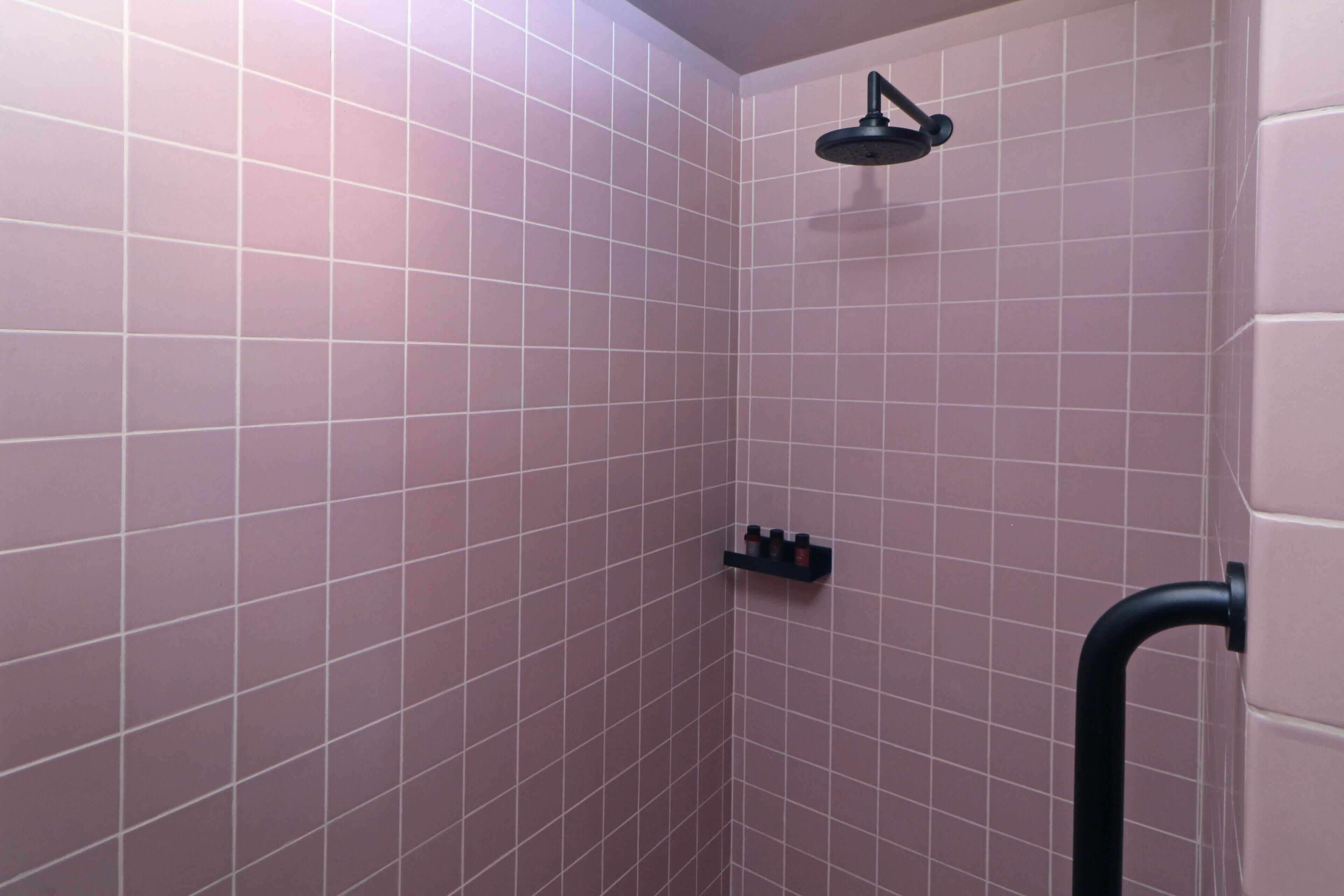 A shower area with pink tiles, a black showerhead, and a black grab bar.