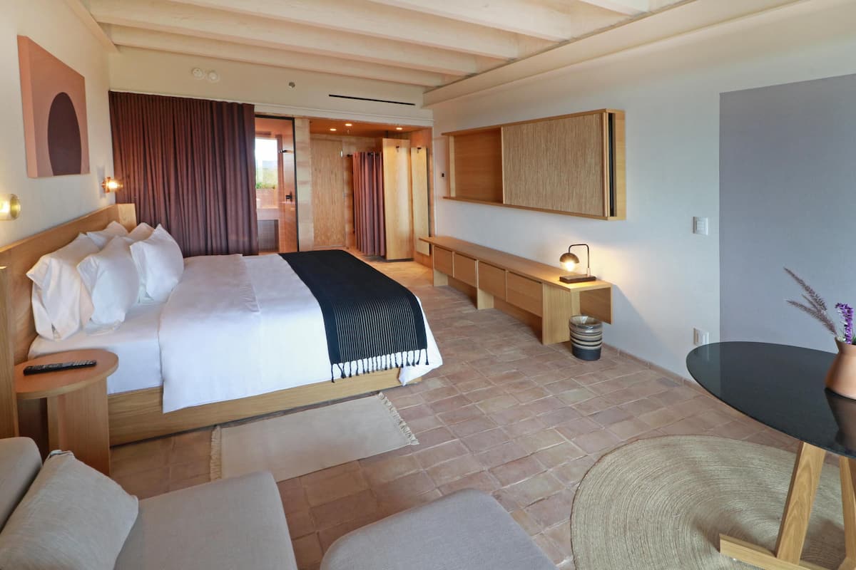 A modern hotel room with a large bed, a desk, a chair, and a small table with a vase of flowers.