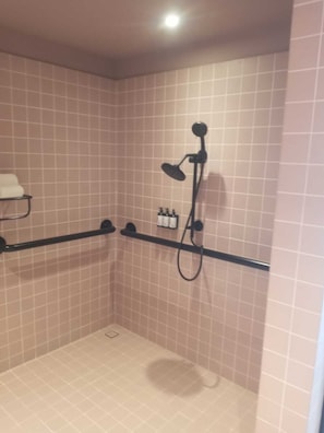 Een kleine douchecel met betegelde wanden, een handdouche en een extra spuitstuk.