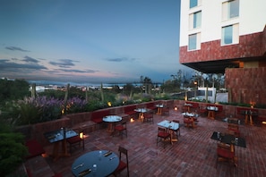 An outdoor patio with multiple tables and chairs, a view of the cityscape, and a building with a red brick facade. - Albor San Miguel de Allende, Tapestry Collection by Hilton (San Miguel de Allende)