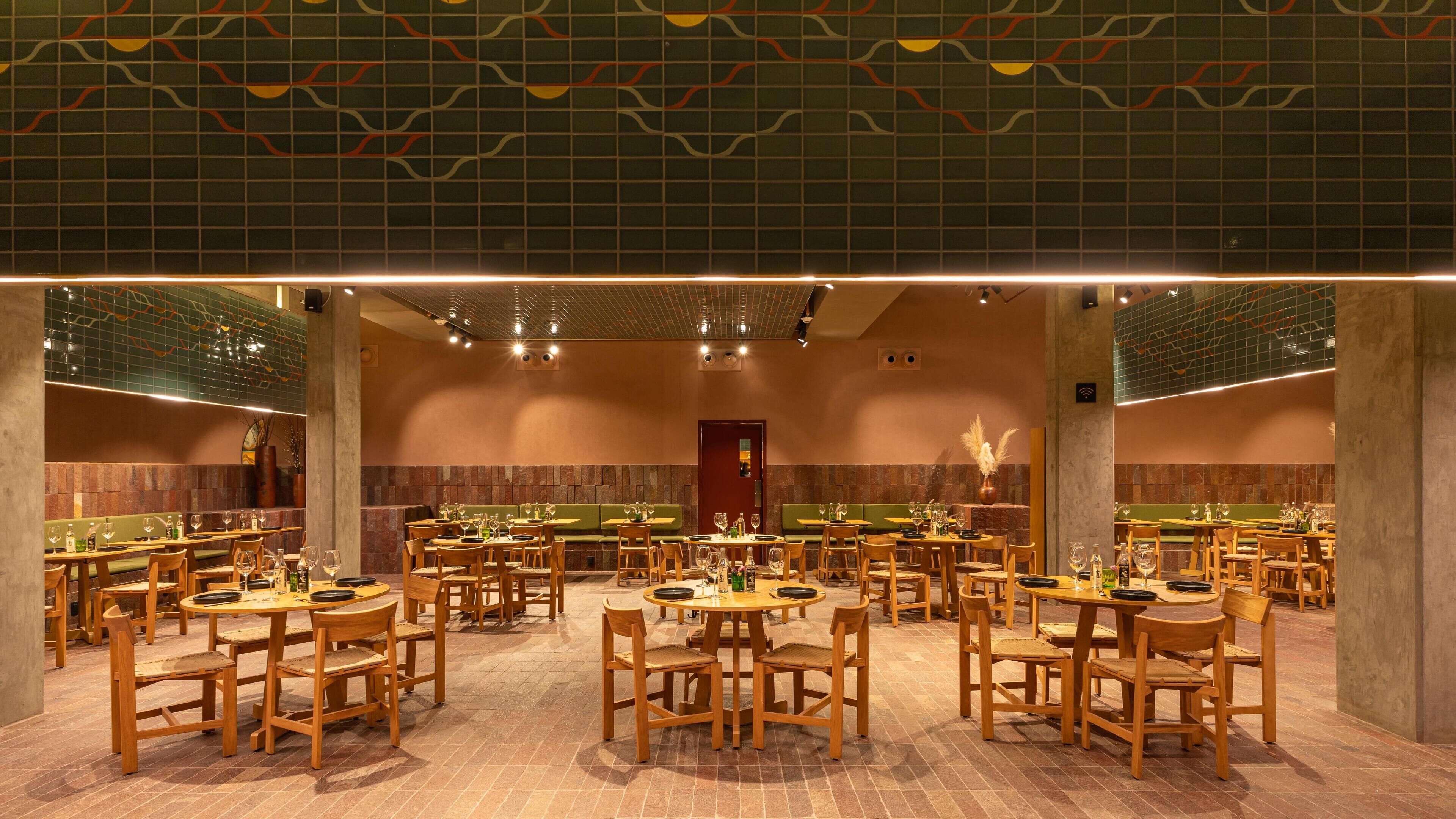 Un restaurante espacioso con varias mesas redondas y sillas de madera, que cuenta con un techo de baldosas y paredes de ladrillo.