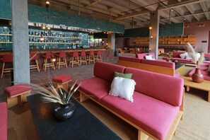 Ein moderner Barbereich mit einer Bar, Hockstühlen und Flaschenregalen. Rote Sofas und ein Couchtisch mit Dekorationselementen sind ebenfalls vorhanden.