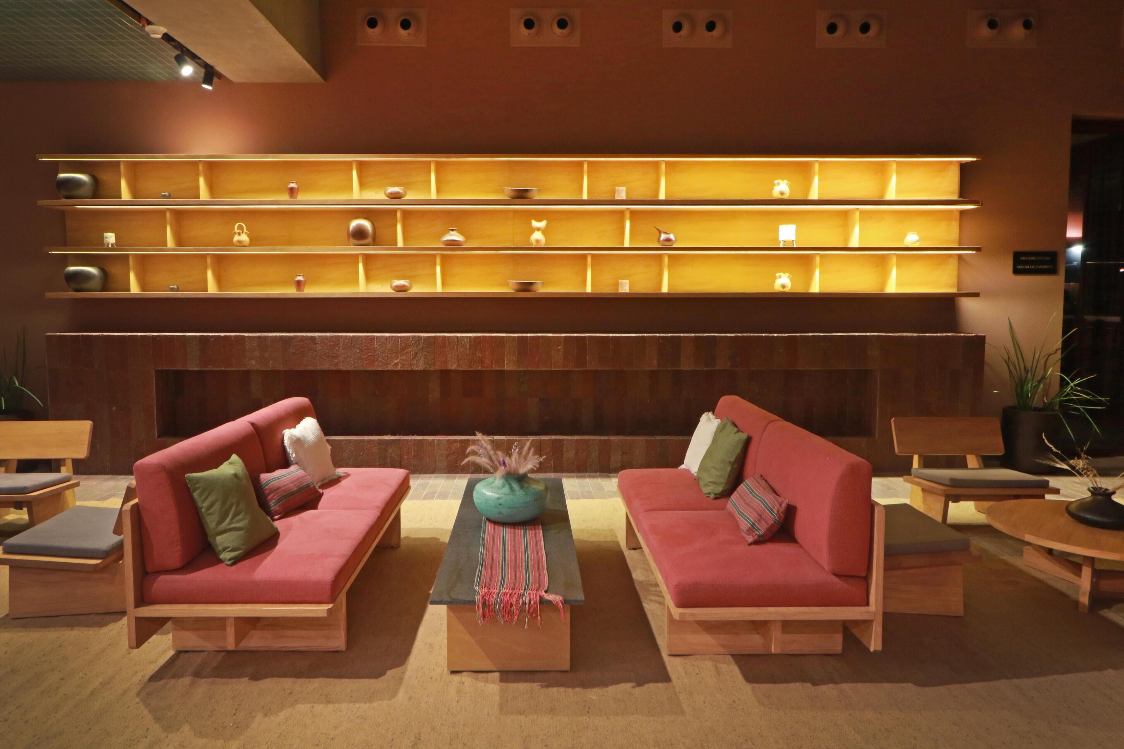 A modern lobby with two red sofas, a central coffee table, and a wall-mounted shelf with various decorative items.