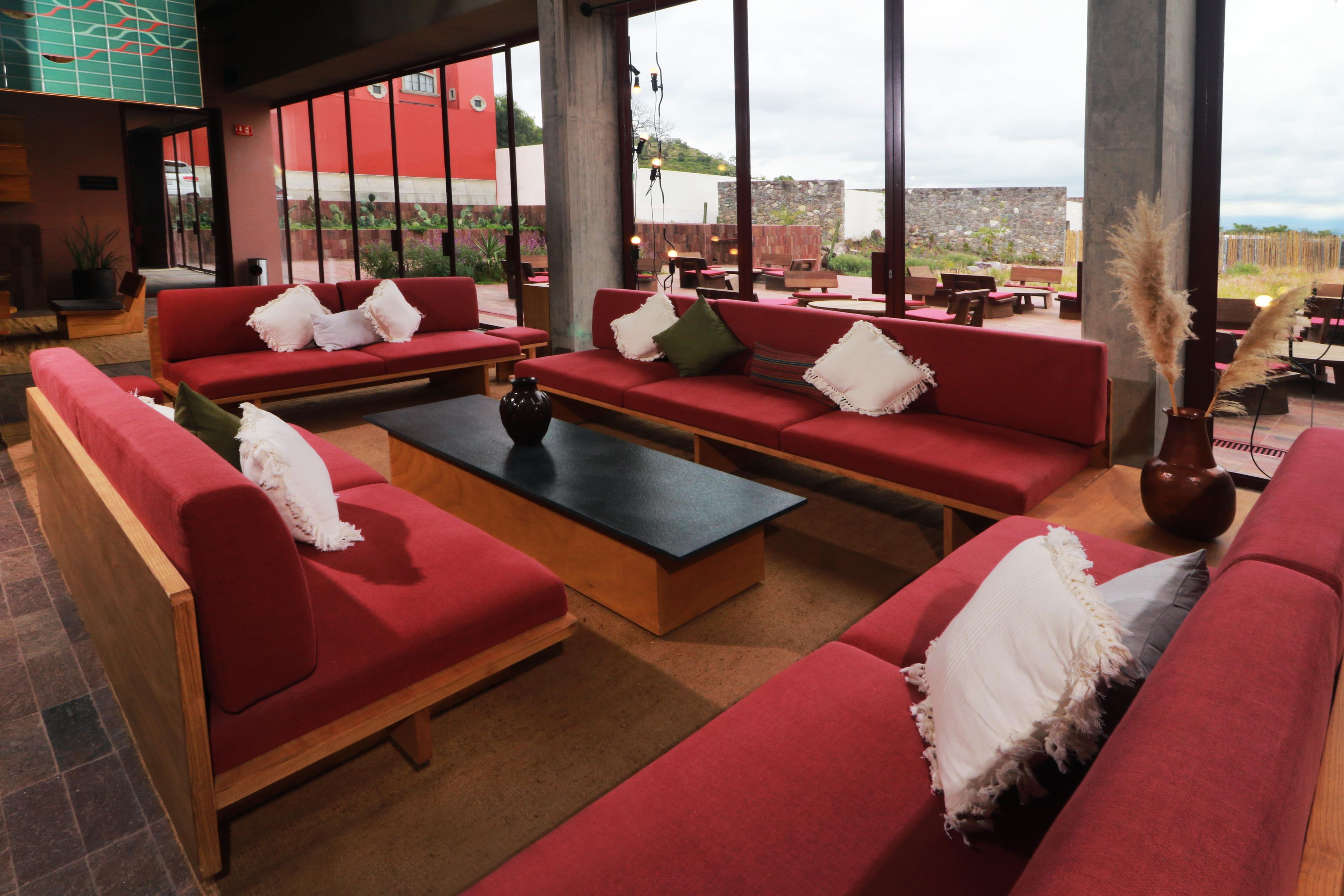 A spacious lounge area with red sofas and a central coffee table, large windows offering a view of the outdoors.