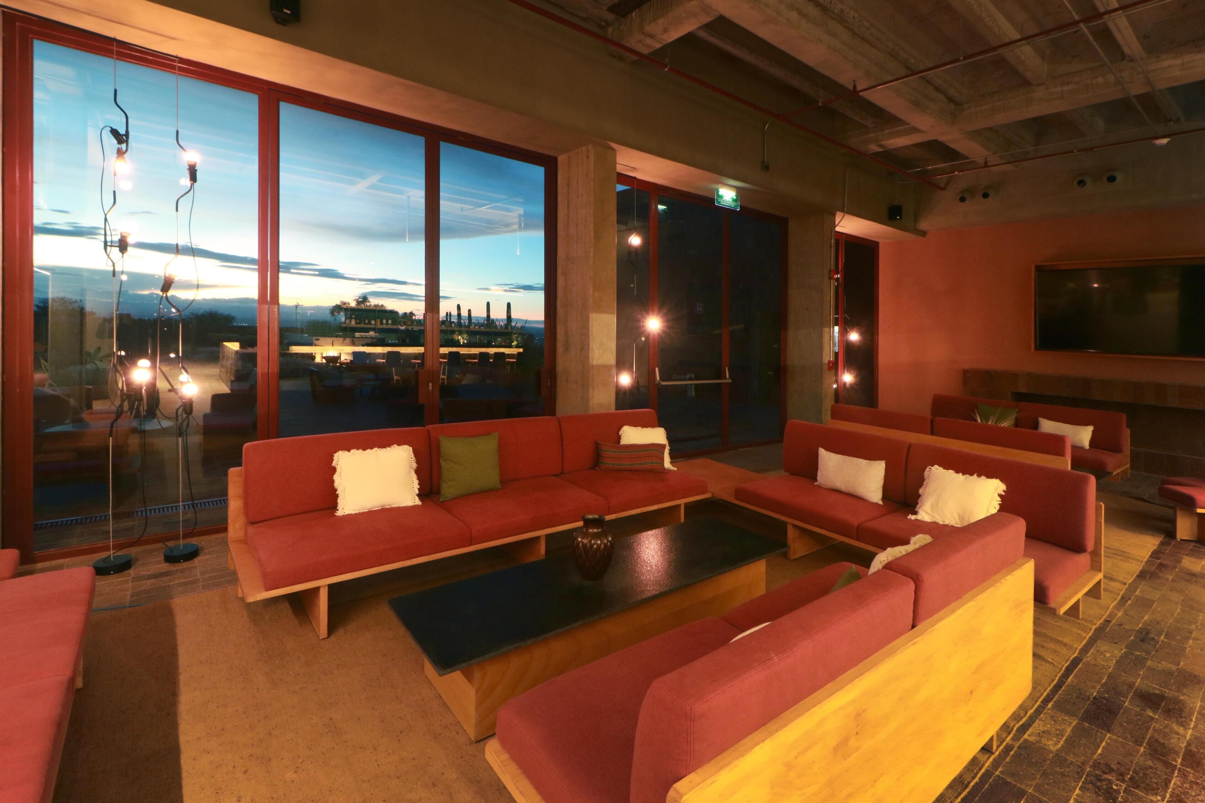 A modern lounge area with red sofas, a black coffee table, and large windows offering a view of the cityscape.