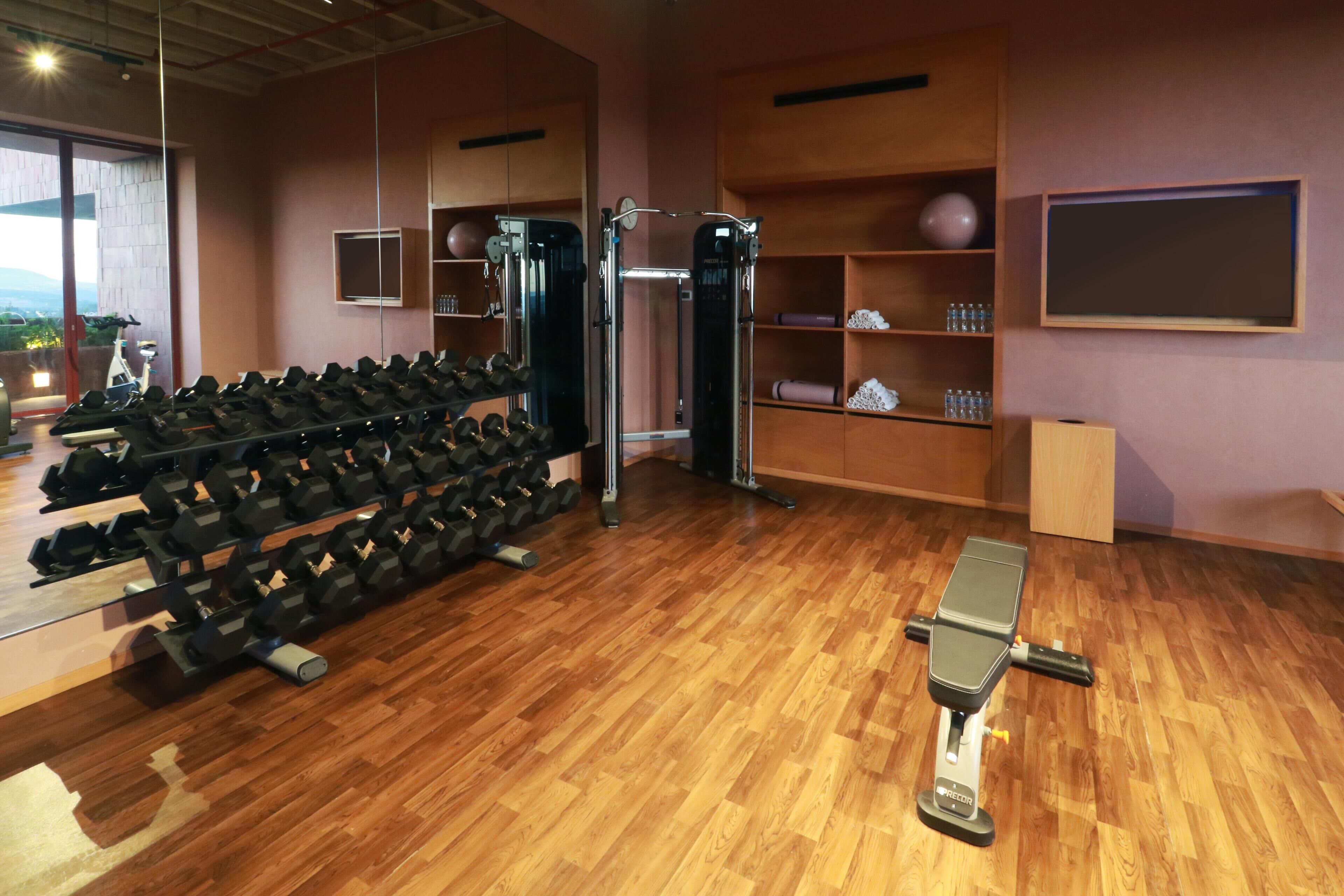 Un gimnasio con suelo de madera, mancuernas, una prensa de banca y diverso equipo de ejercicio.
