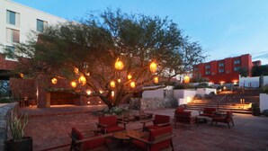 An outdoor patio area with red seating, a large tree, and a staircase leading to a building. - Albor San Miguel de Allende, Tapestry Collection by Hilton (San Miguel de Allende)
