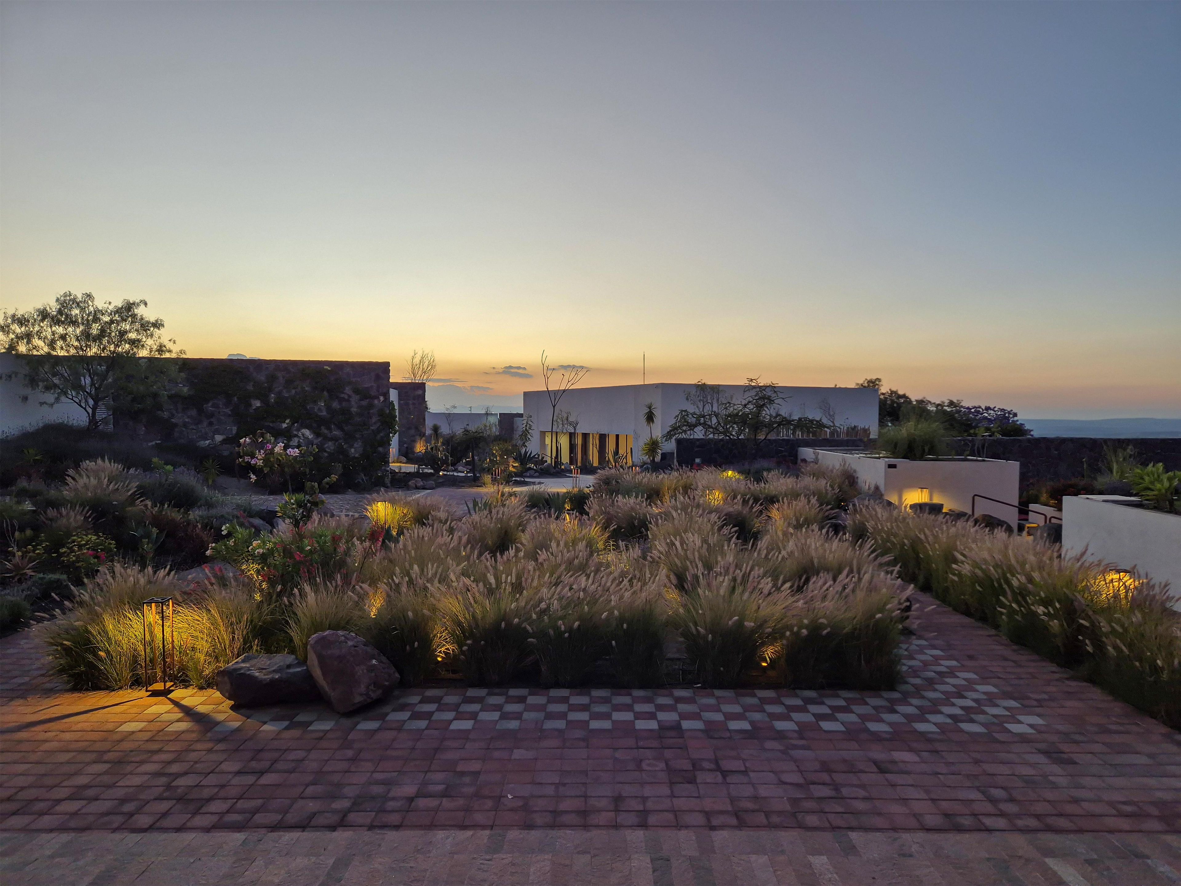A landscaped outdoor area with a paved walkway, a modern building, and a view of the horizon.