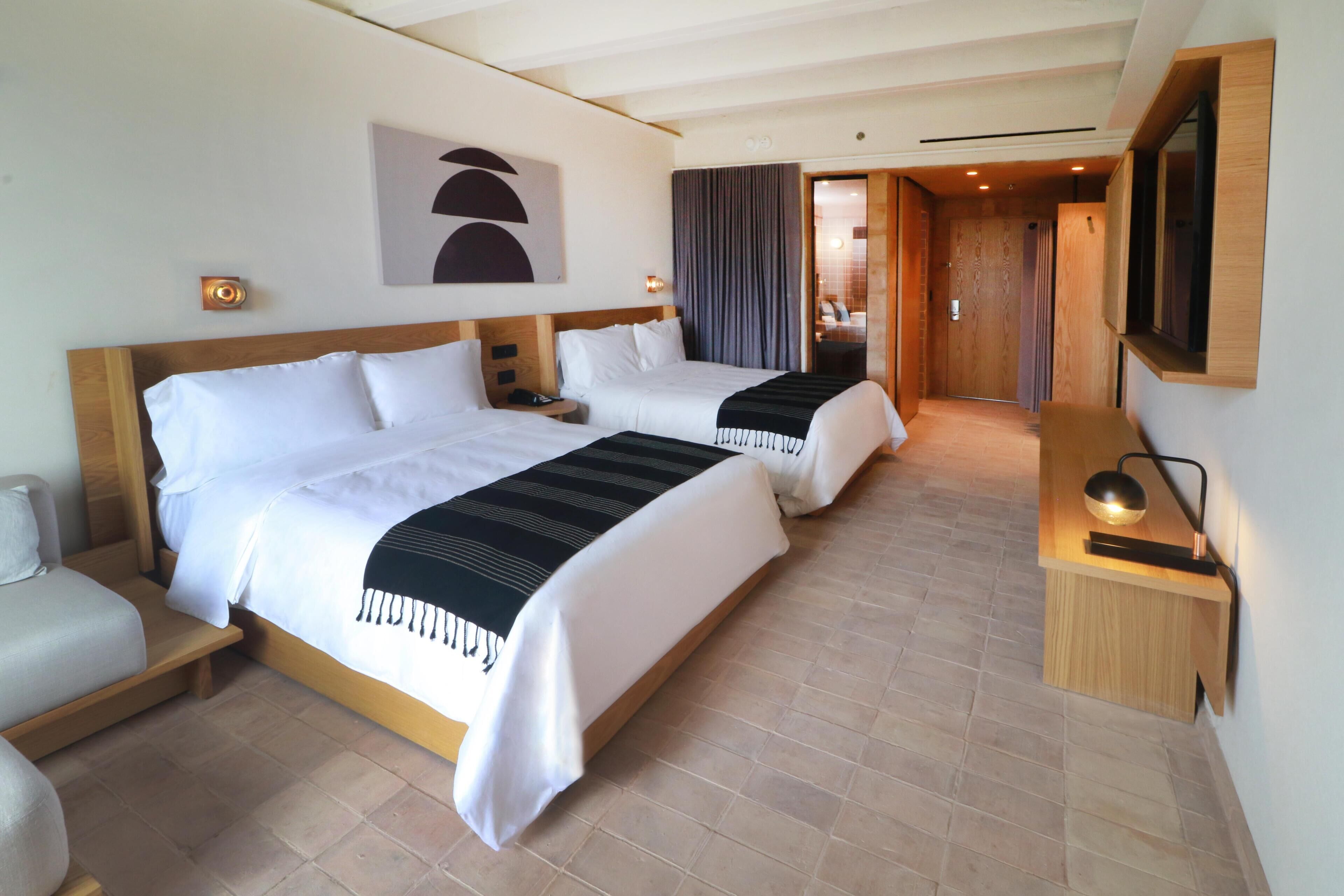 A hotel room with two beds, a desk, and a bathroom visible through an open door.
