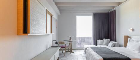 A modern hotel room with a bed, bedside table, bench, and a view of the outdoors.