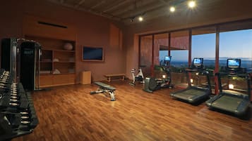 A gym with exercise equipment, a wooden floor, and a large window with a view.