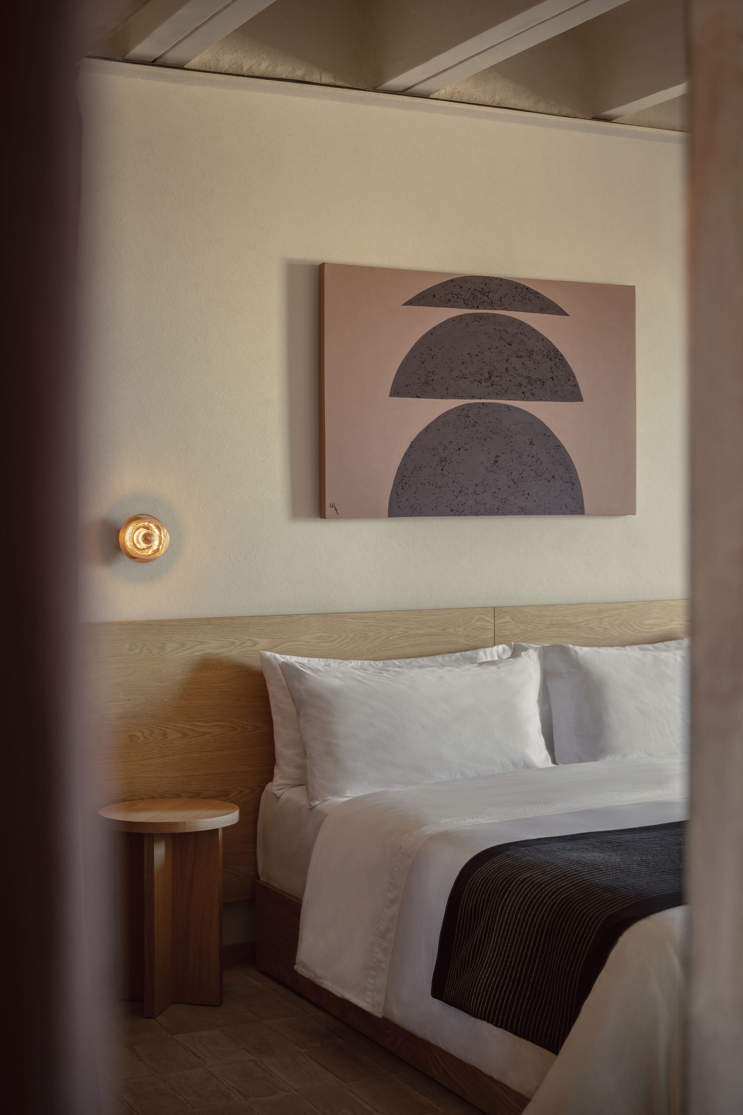 Un dormitorio con una cama, una mesita de noche, una lámpara de pared y una obra de arte abstracta.