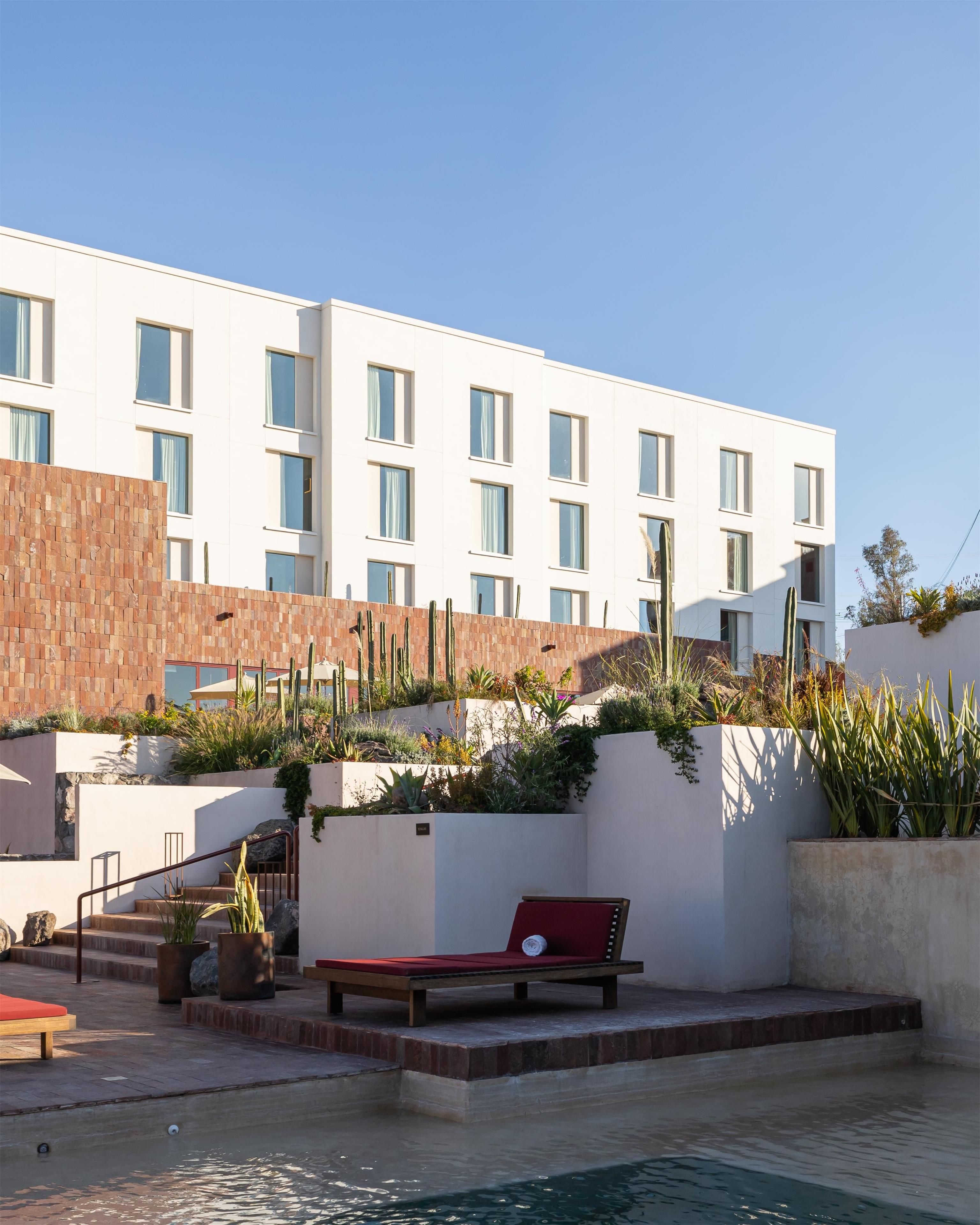 A modern building with a pool area, including a red lounge chair and various plants.