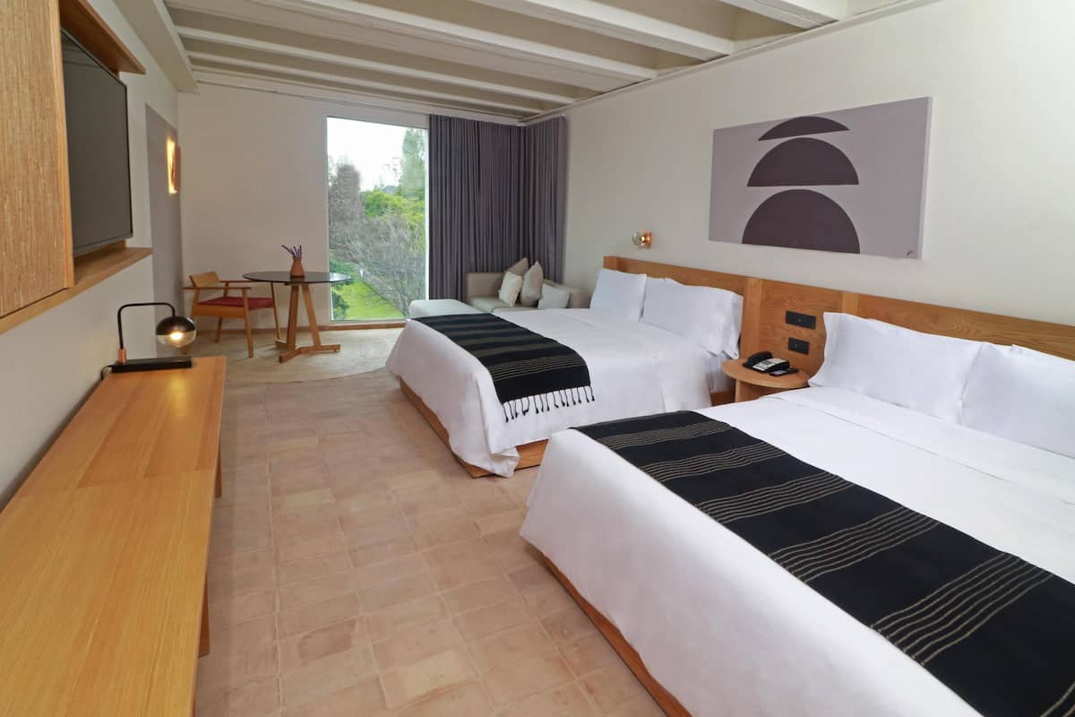 A hotel room with two beds, a TV, a desk, and a view of the outdoors.