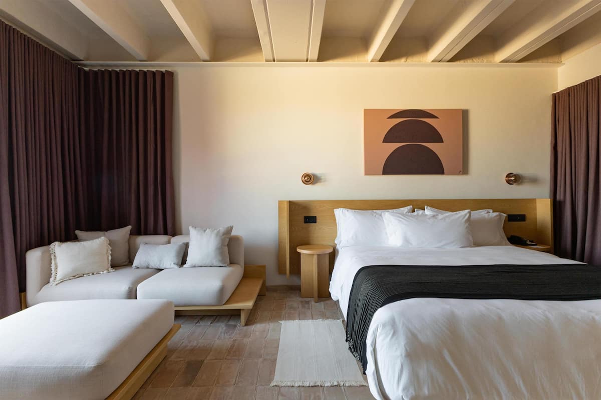 A hotel room with a bed, a sofa, a small table, and a wall-mounted artwork.