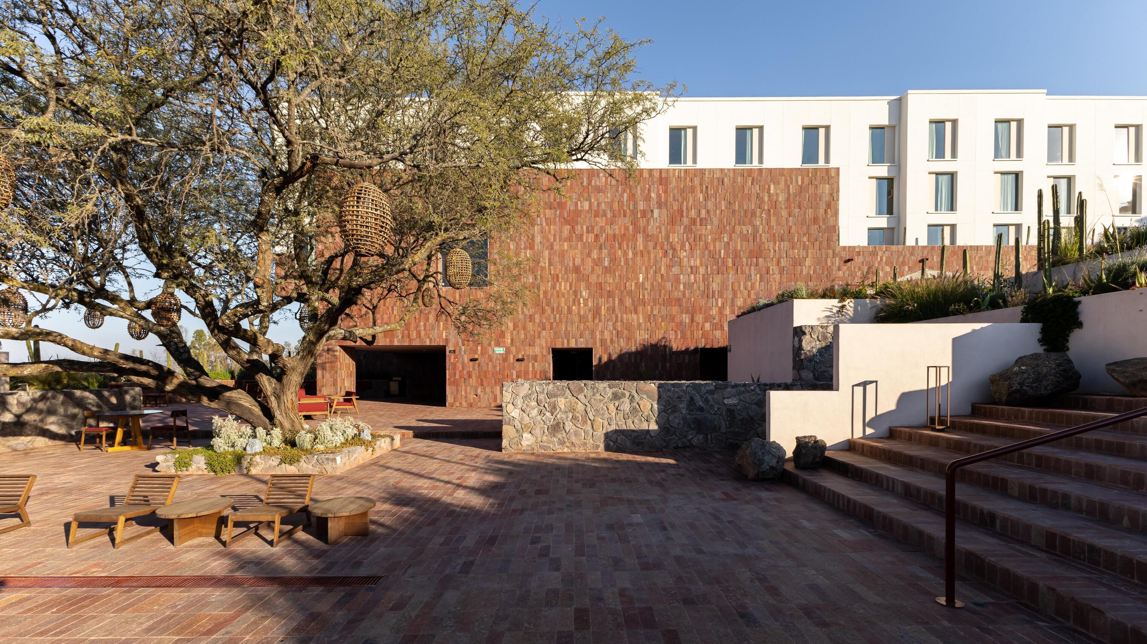 An outdoor patio area with wooden furniture, a stone wall, and a building with a wooden facade.