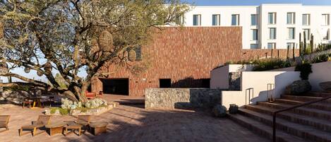 An outdoor patio area with wooden furniture, a stone wall, and a building with a wooden facade.