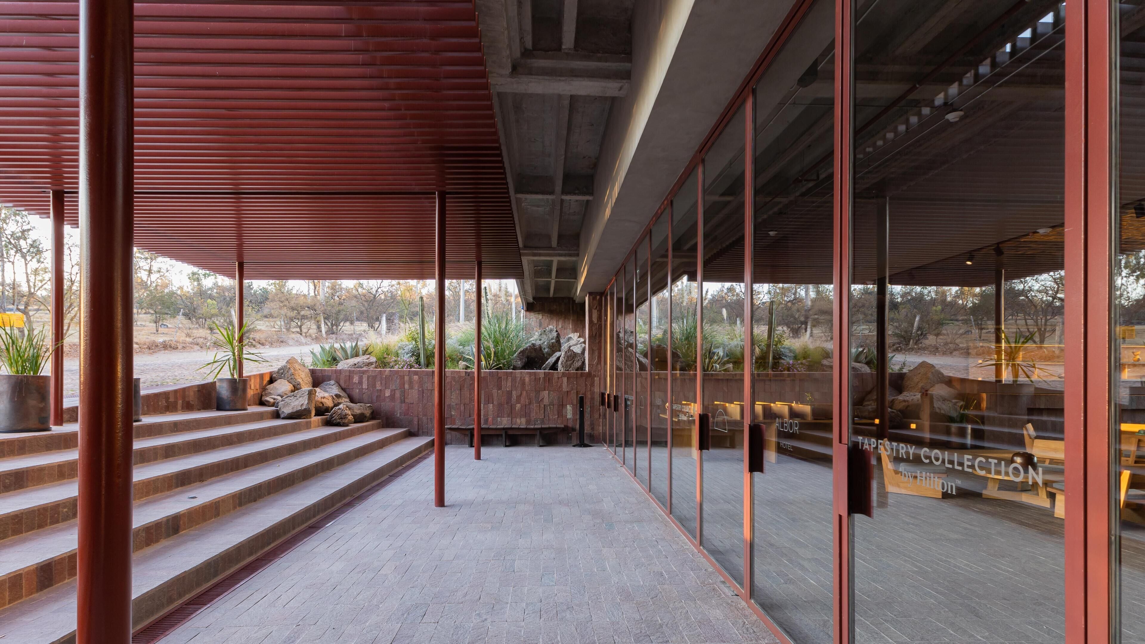 Um lobby de hotel moderno com uma parede de pedra, uma escadaria que leva a um andar superior e vista para a paisagem ao redor.