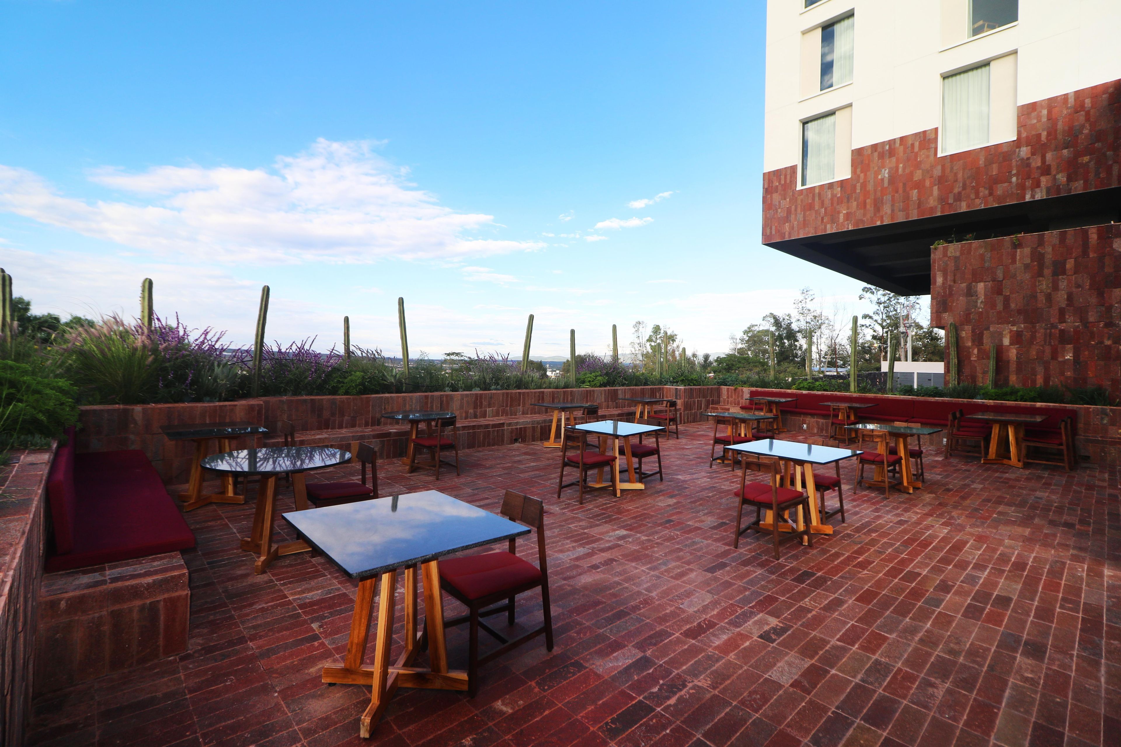 An outdoor patio with multiple tables and chairs, a brick floor, and a view of the cityscape.