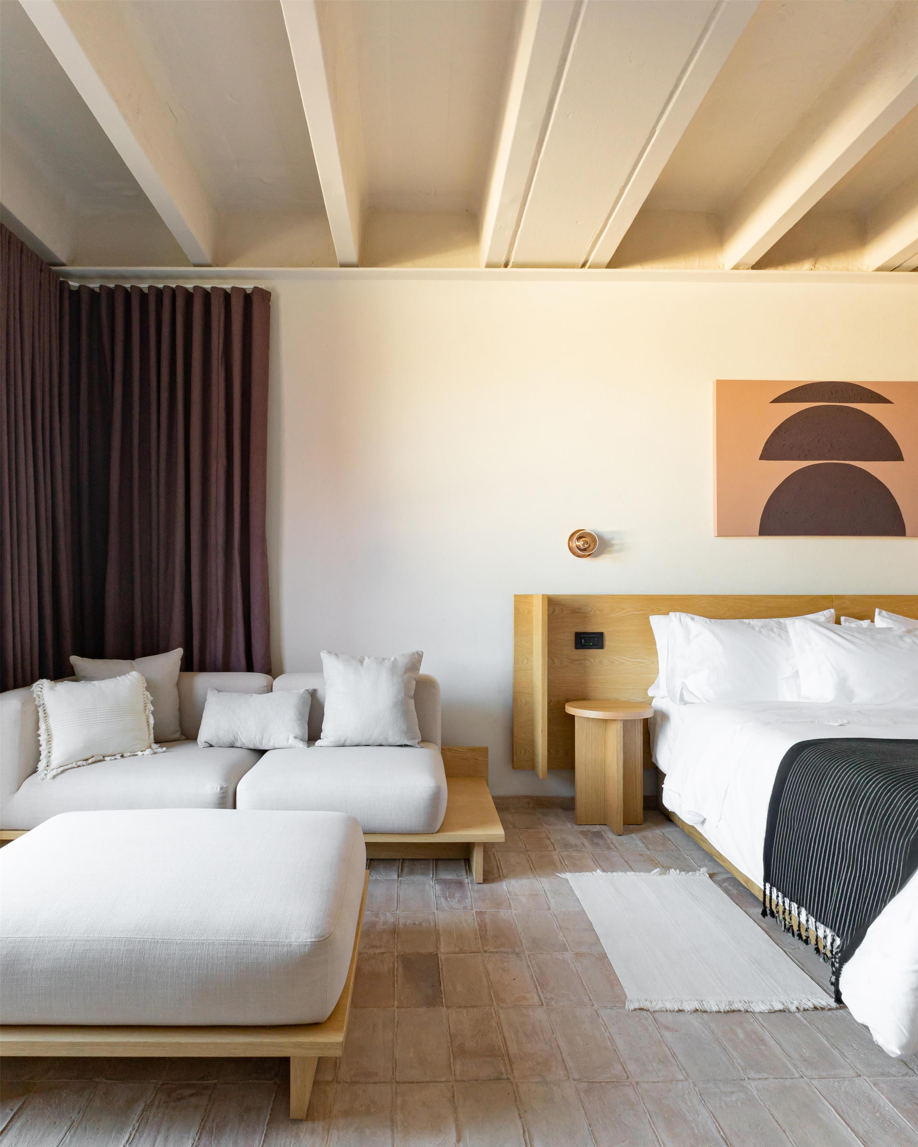 A hotel room with a bed, a sofa, a small table, and a wall-mounted artwork.
