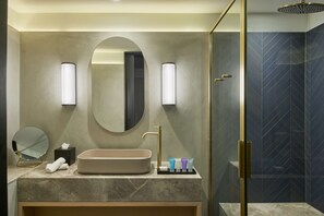 Un baño moderno con un espejo ovalado grande, un lavabo color beige y una ducha con mampara de vidrio.