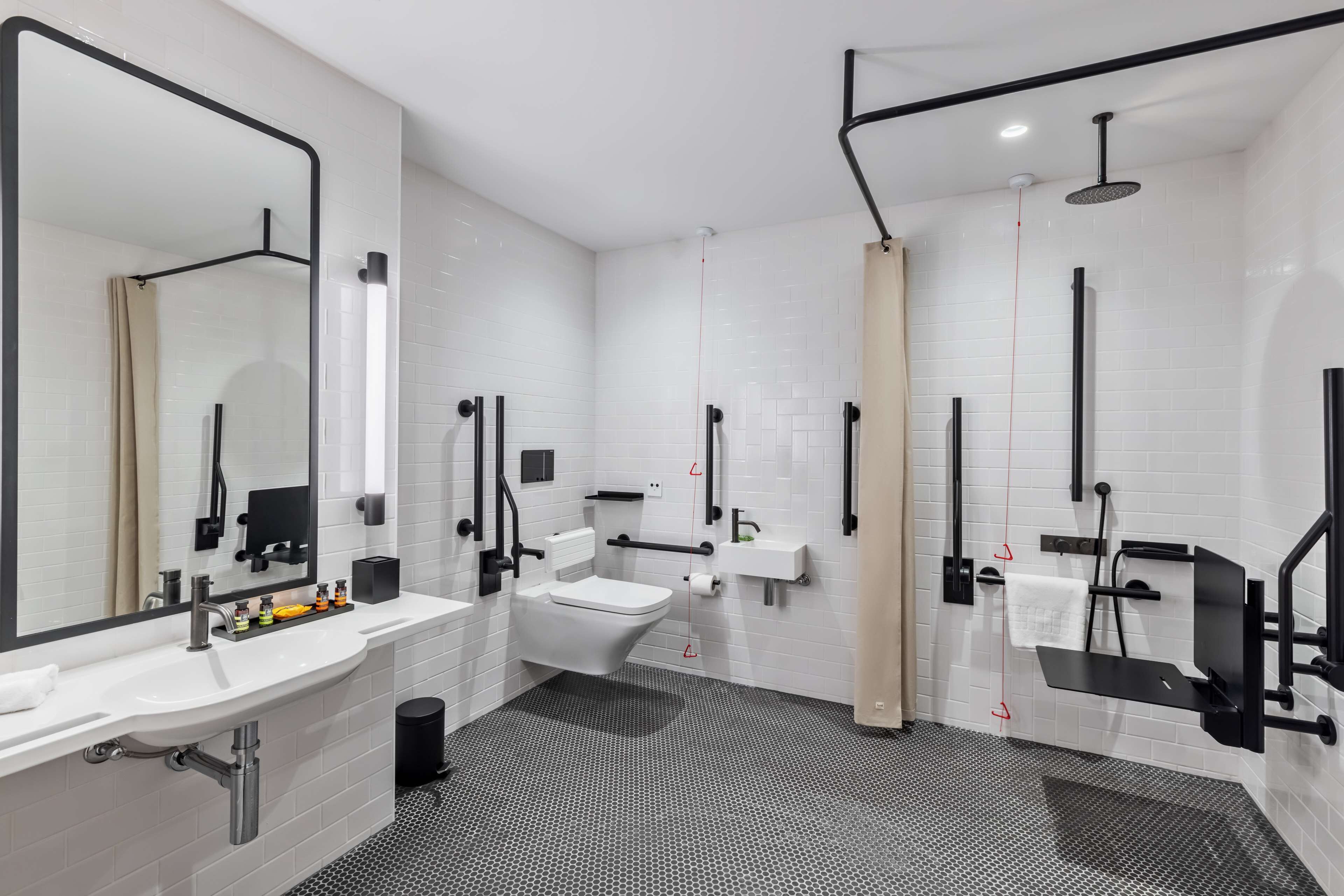 A modern bathroom with a large mirror, two sinks, a toilet, and a shower area.