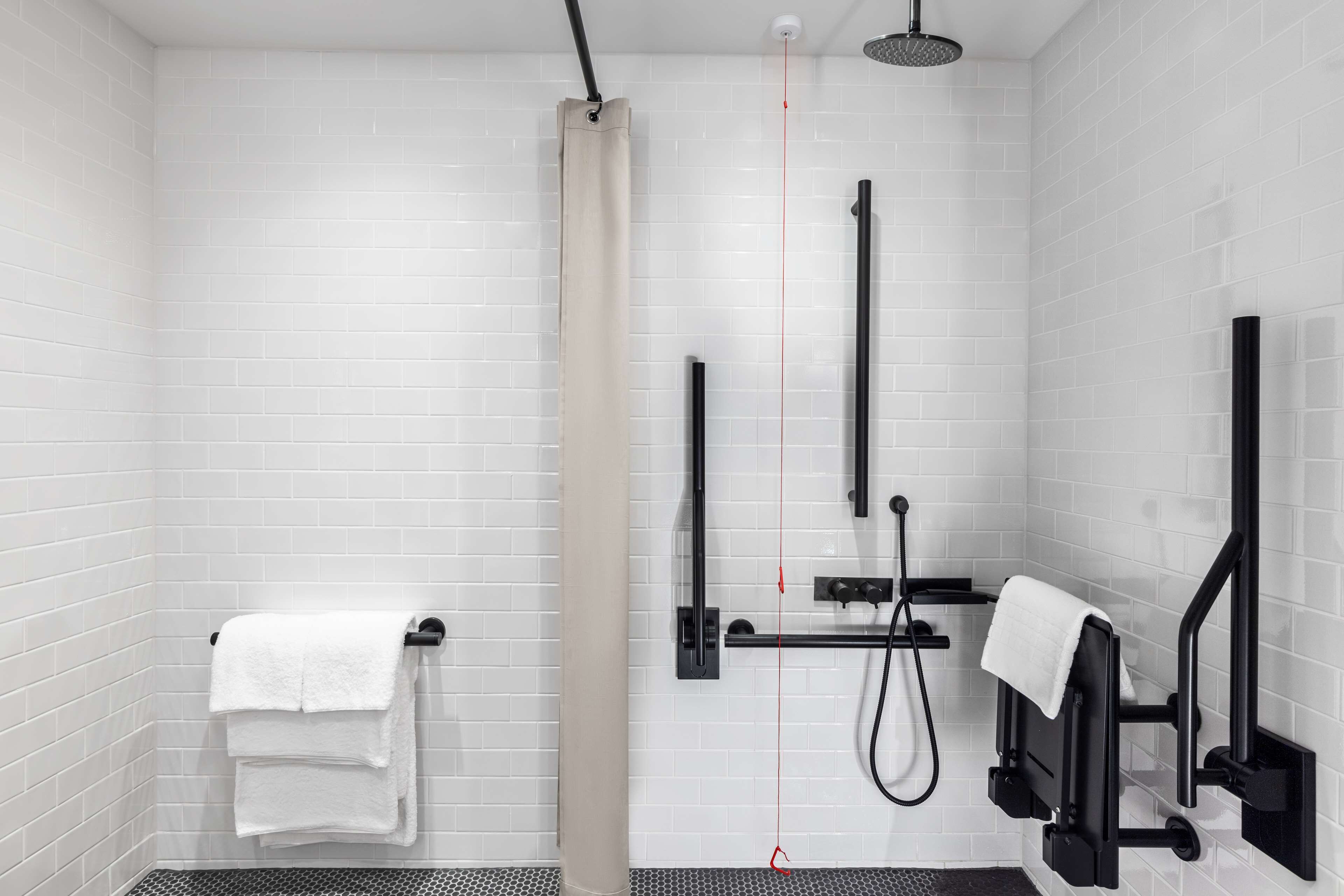 Une salle de bain moderne avec des murs recouverts de carreaux blancs, un rideau de douche beige, un porte-serviettes noir et une serviette noire qui y est accrochée.