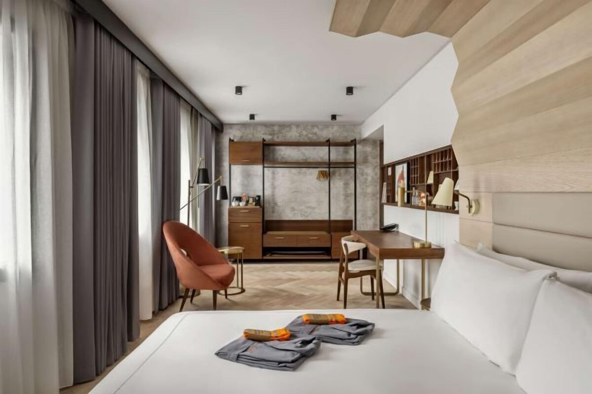 A modern hotel room with a bed, a desk, a chair, and a wardrobe.