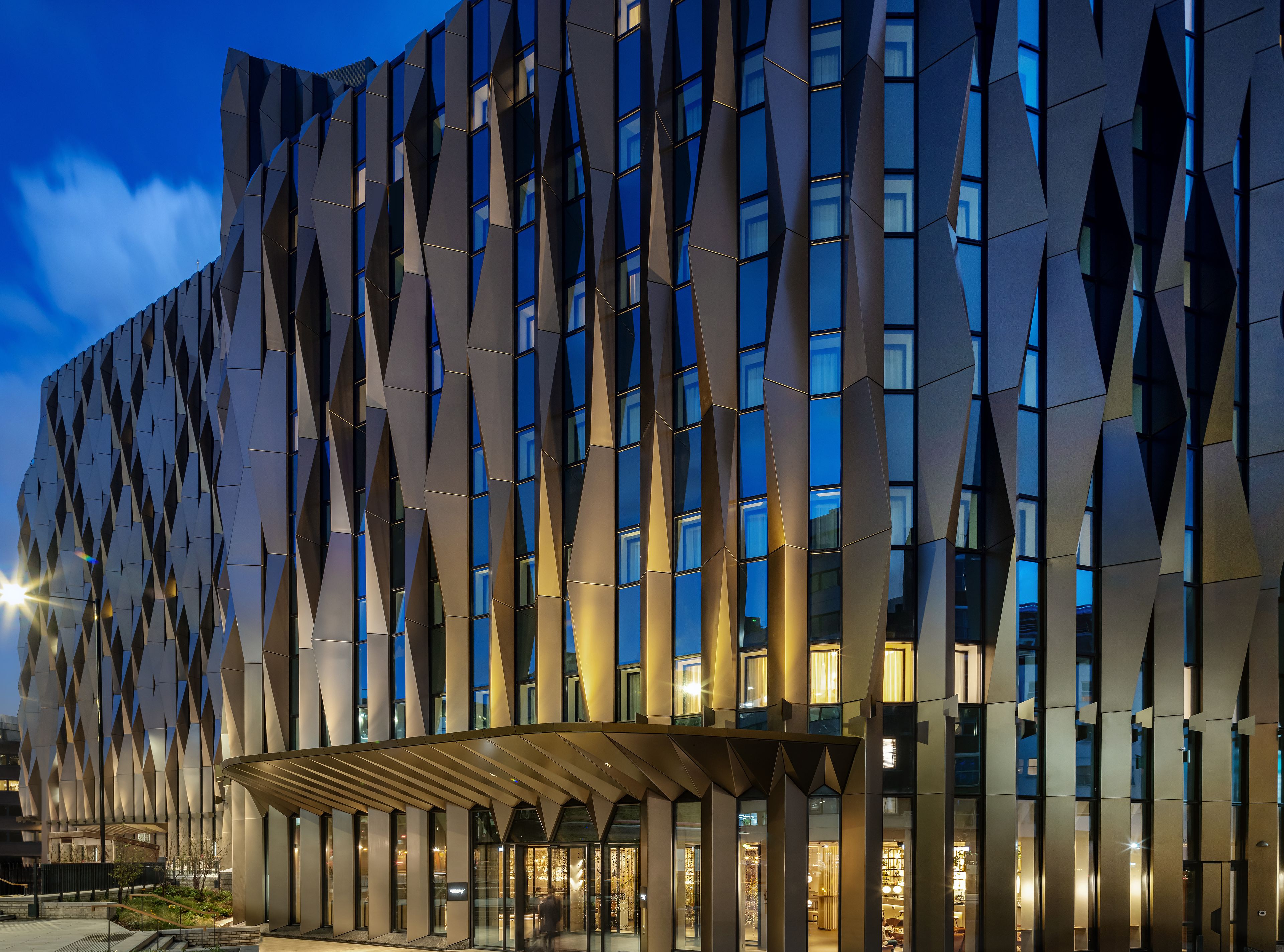 Un bâtiment moderne doté d’une façade géométrique et de fenêtres illuminées.