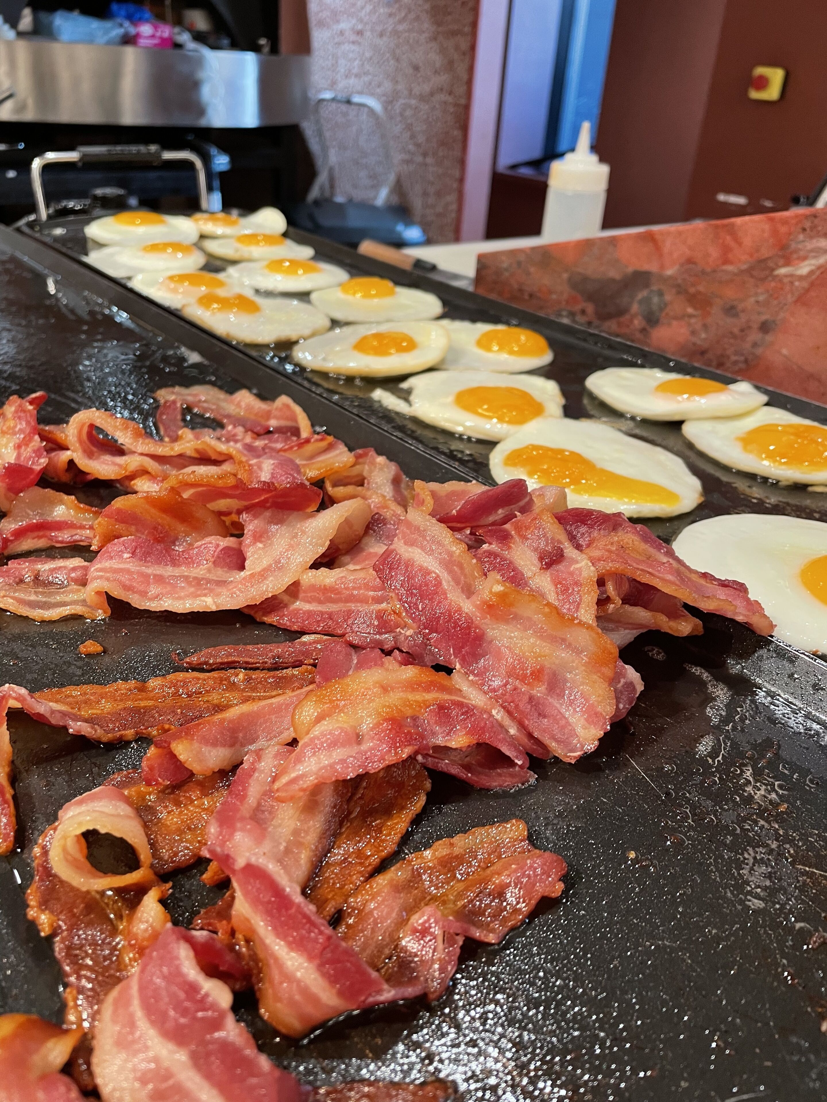 A breakfast setup with eggs and bacon on a griddle.