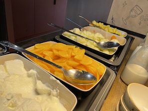Un bufé con diversos alimentos, incluyendo rodajas de naranja, trozos de melón y un recipiente de crema batida.