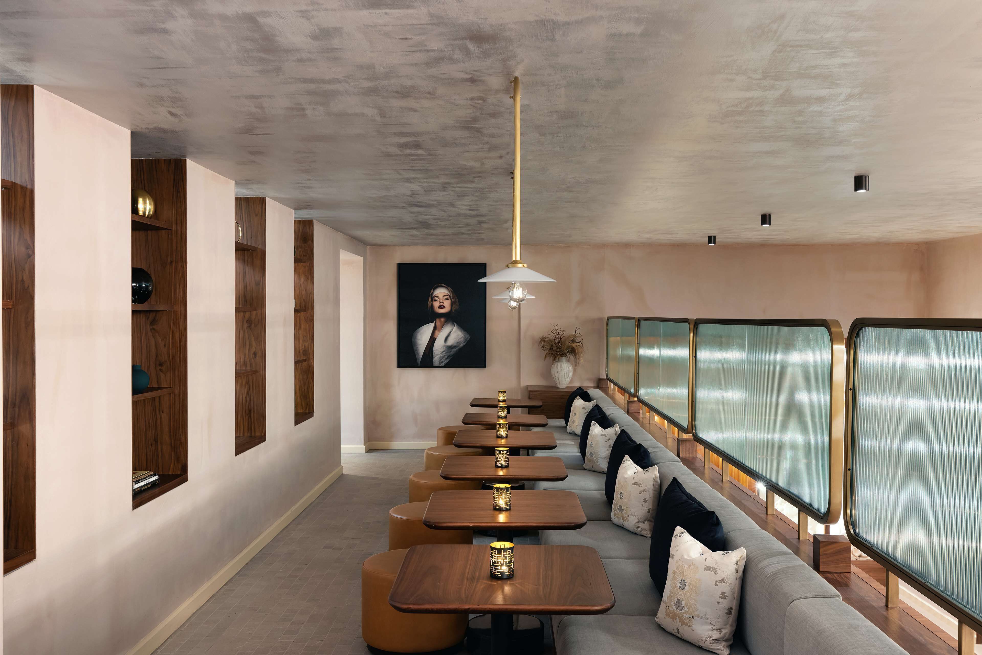 A modern interior with a row of wooden tables and a sofa along a wall with frosted glass panels.