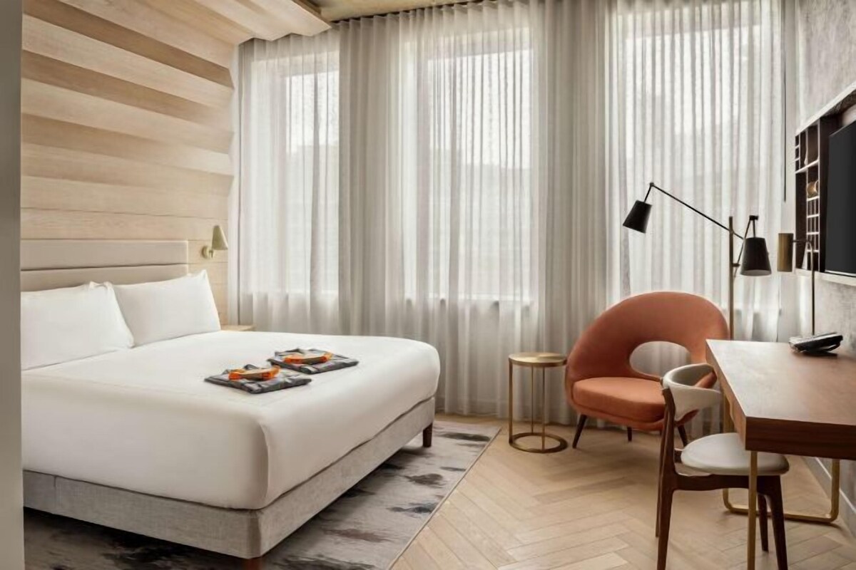 Habitación de hotel moderna con una cama grande, una mesita redonda pequeña, una silla y un escritorio.